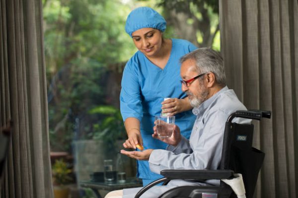 Female nurse giving medicine to disabled old man on wheelchair