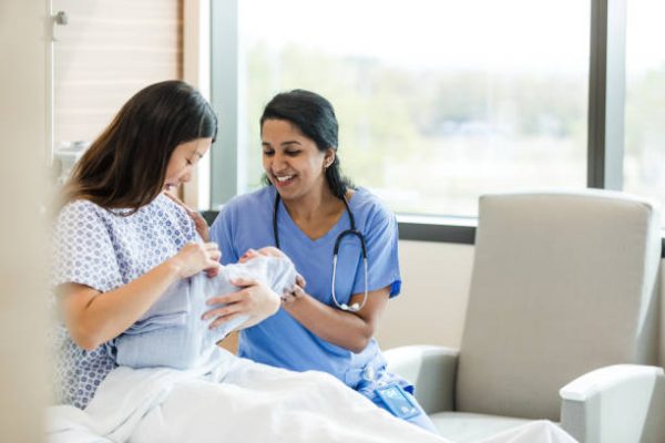 The female doctor sits bedside with the new mother to answer her questions about her newborn baby.